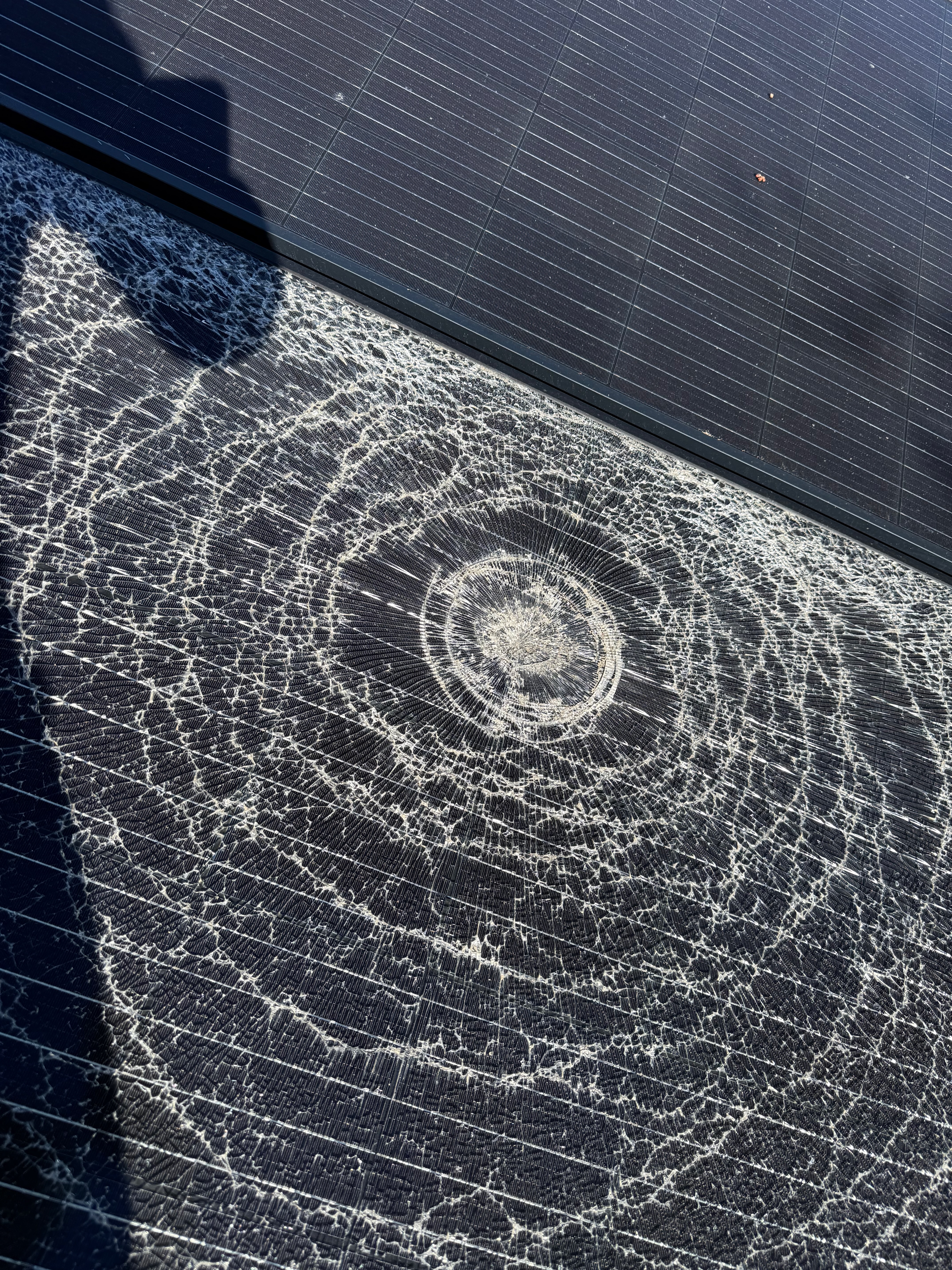 Circular hailstone impact with fractures across the solar panel glass